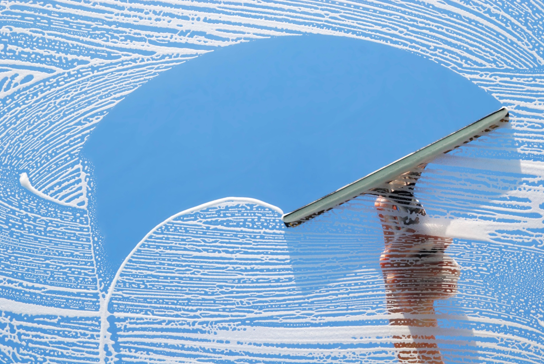 Professional squeegee cleaning a sparkling clean window with sky reflection